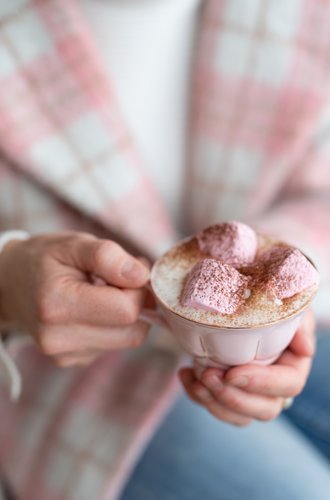 Person holding a mug of hot chocolate with pink marshmallows against a plaid background